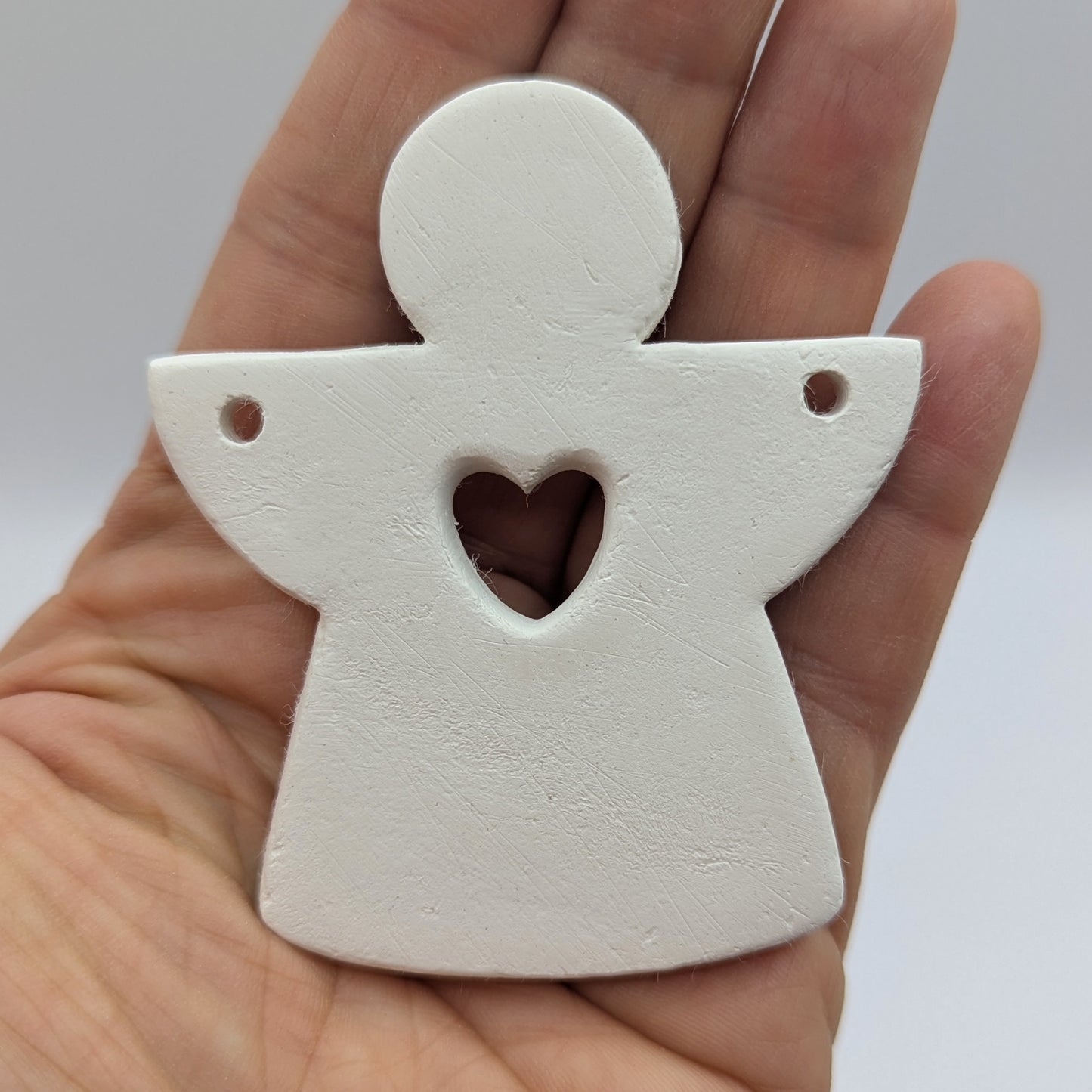 White clay angel ornament with a heart cut out, held in a hand