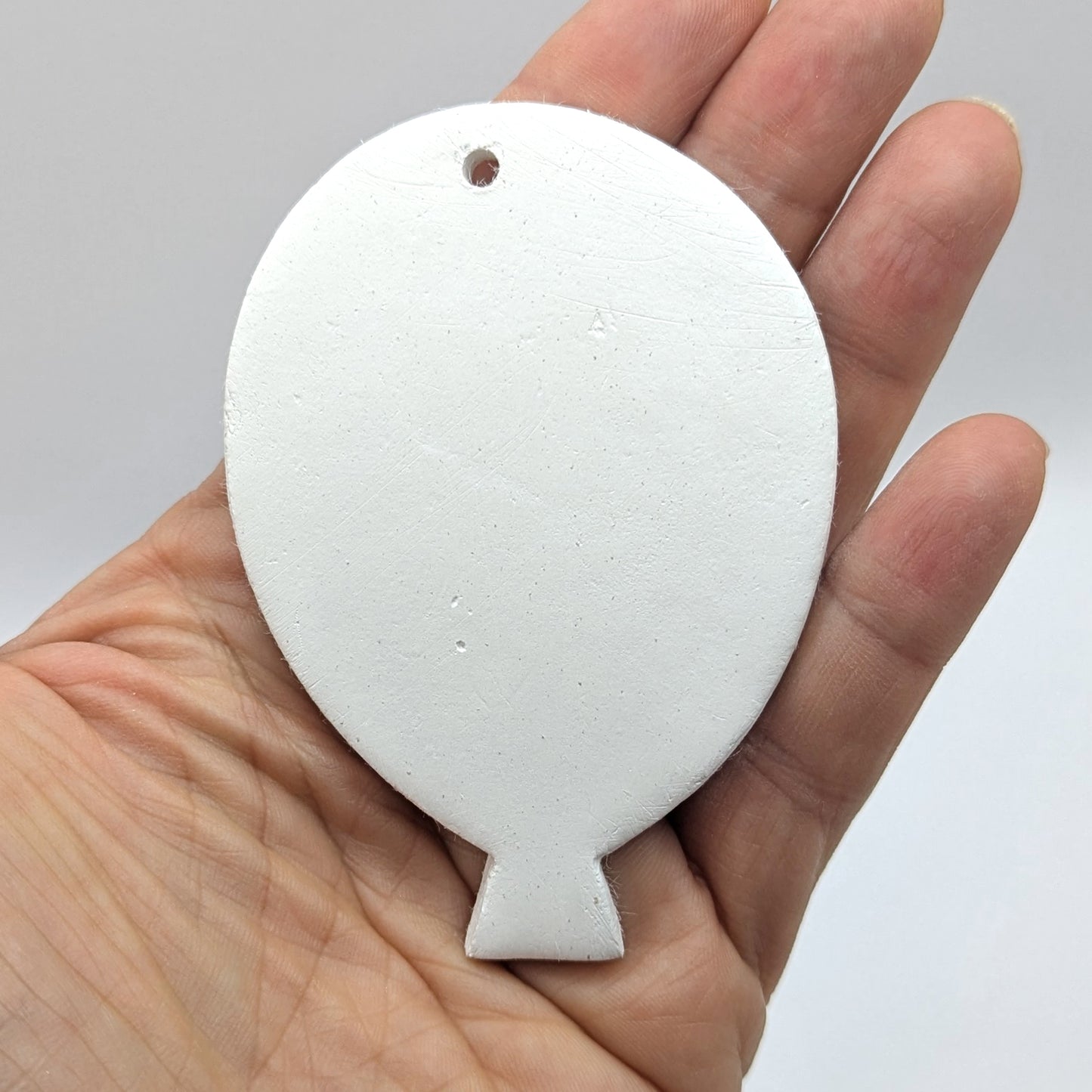 White clay balloon decoration / tag / ornament held in a hand