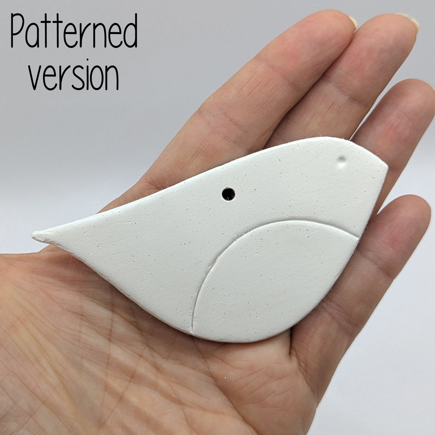 Robin shaped white clay bird decoration, with chest and eye stamped in, held in hand to show scale