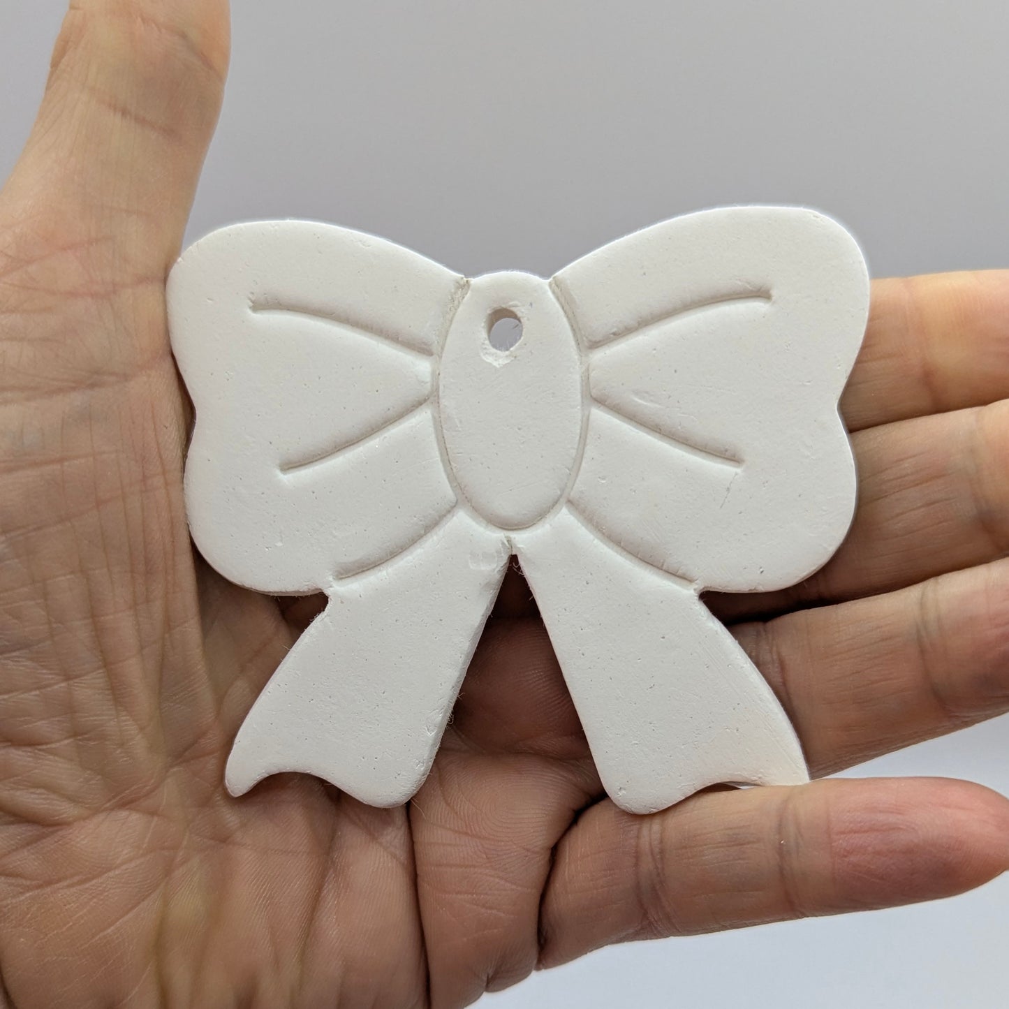 white bow shaped clay decoration held in a hand for size