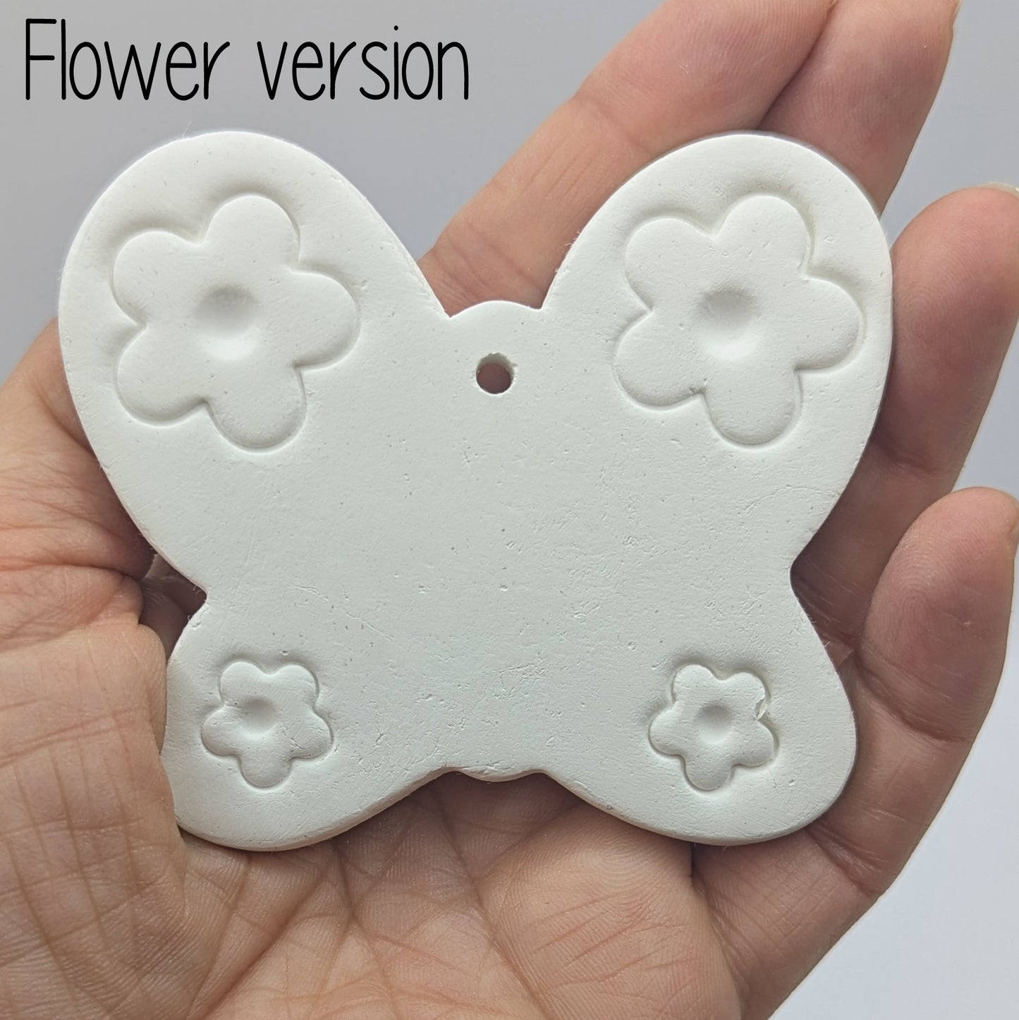 small air dried clay butterfly decoration, with a flower pattern stamped into the wings, in a ladies hand to show scale