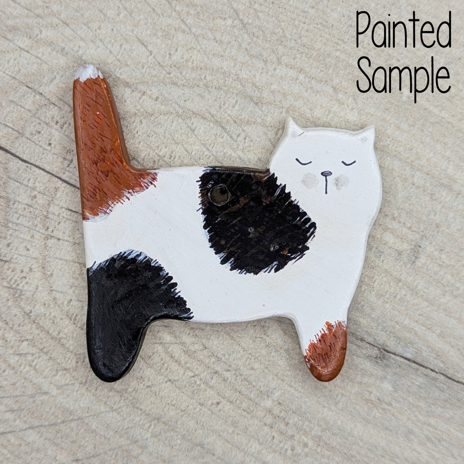 side view of a cat, clay decoration, painted with black and mid brown splodges and a cute cat face