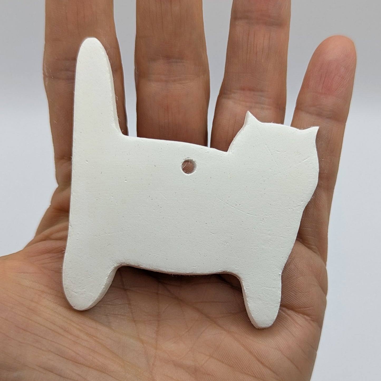 side view of cat, air dried clay decoration to paint and decorate being held in palm of hand to show size