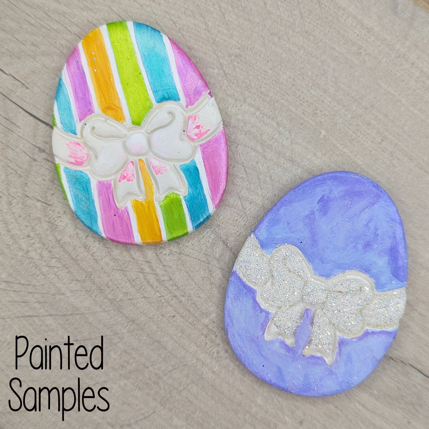 Two painted easter egg clay decorations with colorful stripes and a bow