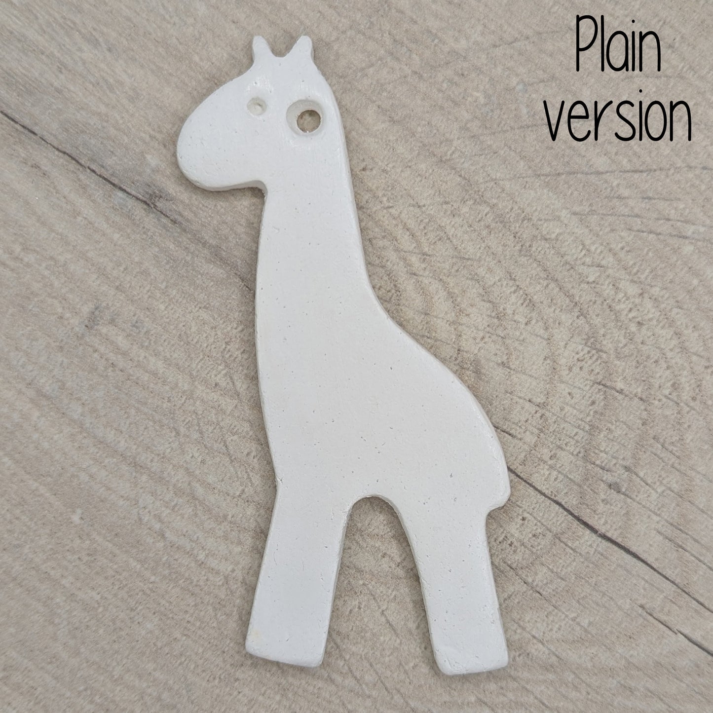 White giraffe shaped clay decoration on a wooden surface, plain version other than an eye stamped in