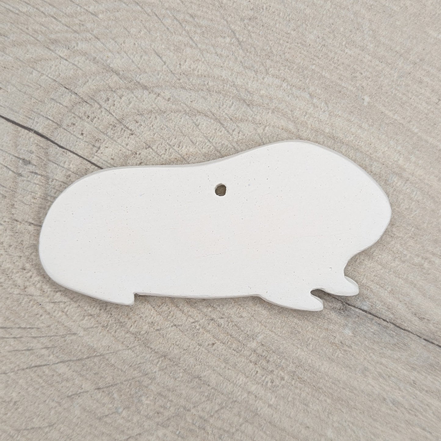 white air dried clay guinea pig shaped decoration on wooden background to paint at home