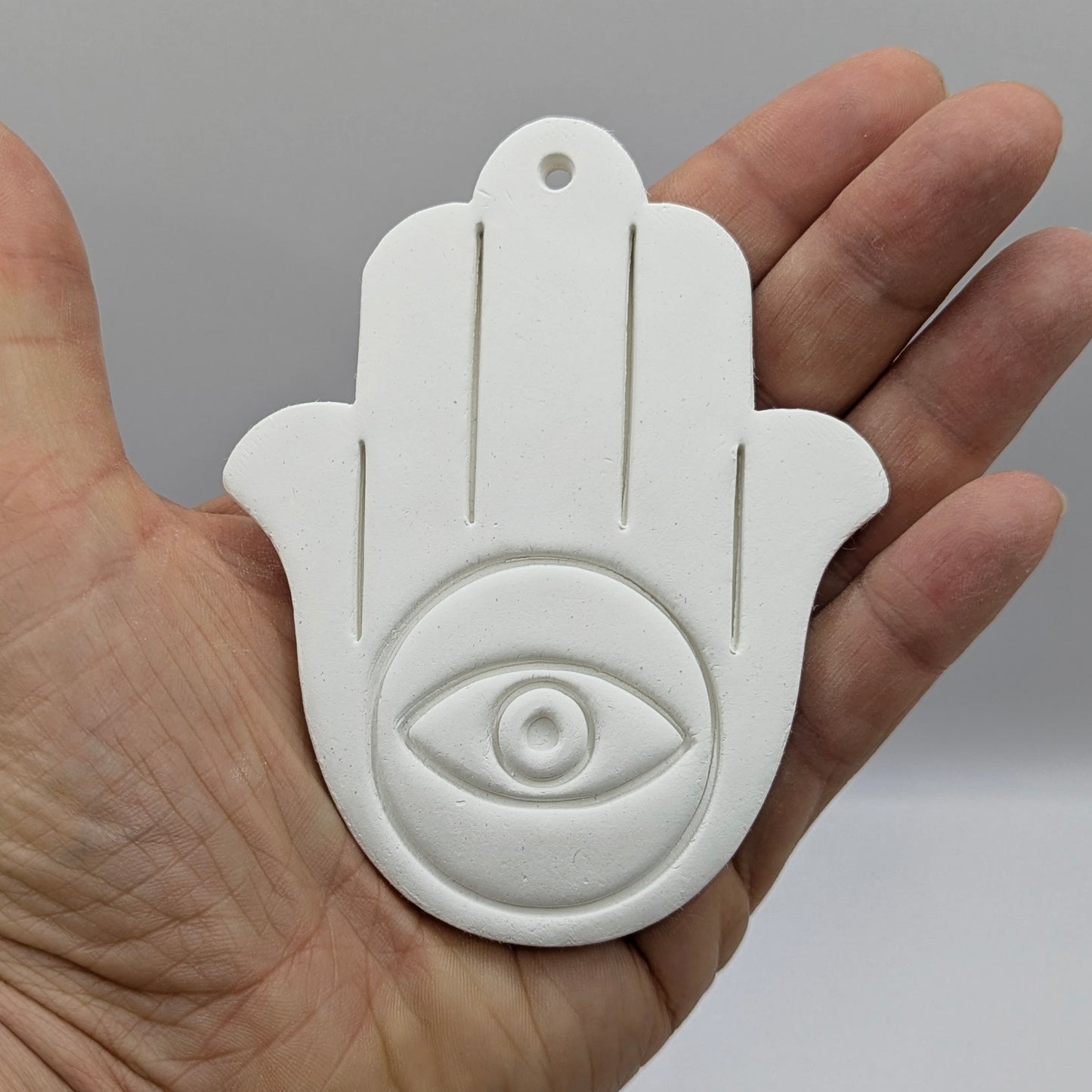 White Hamsa hand with eye design held in a hand against a gray background