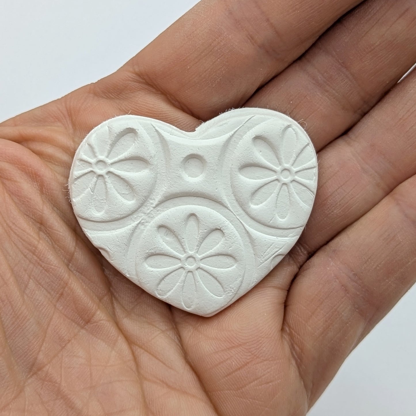 small patterned clay decoration in palm of hand to show size