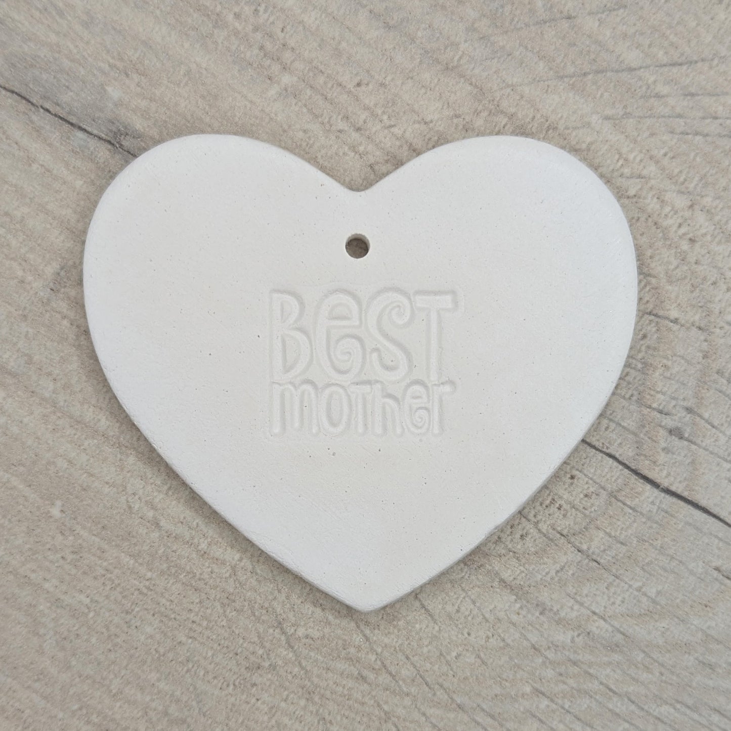 Heart shaped air dried clay decoration / tag with 'Best mother' stamped into the clay, on a wooden surface