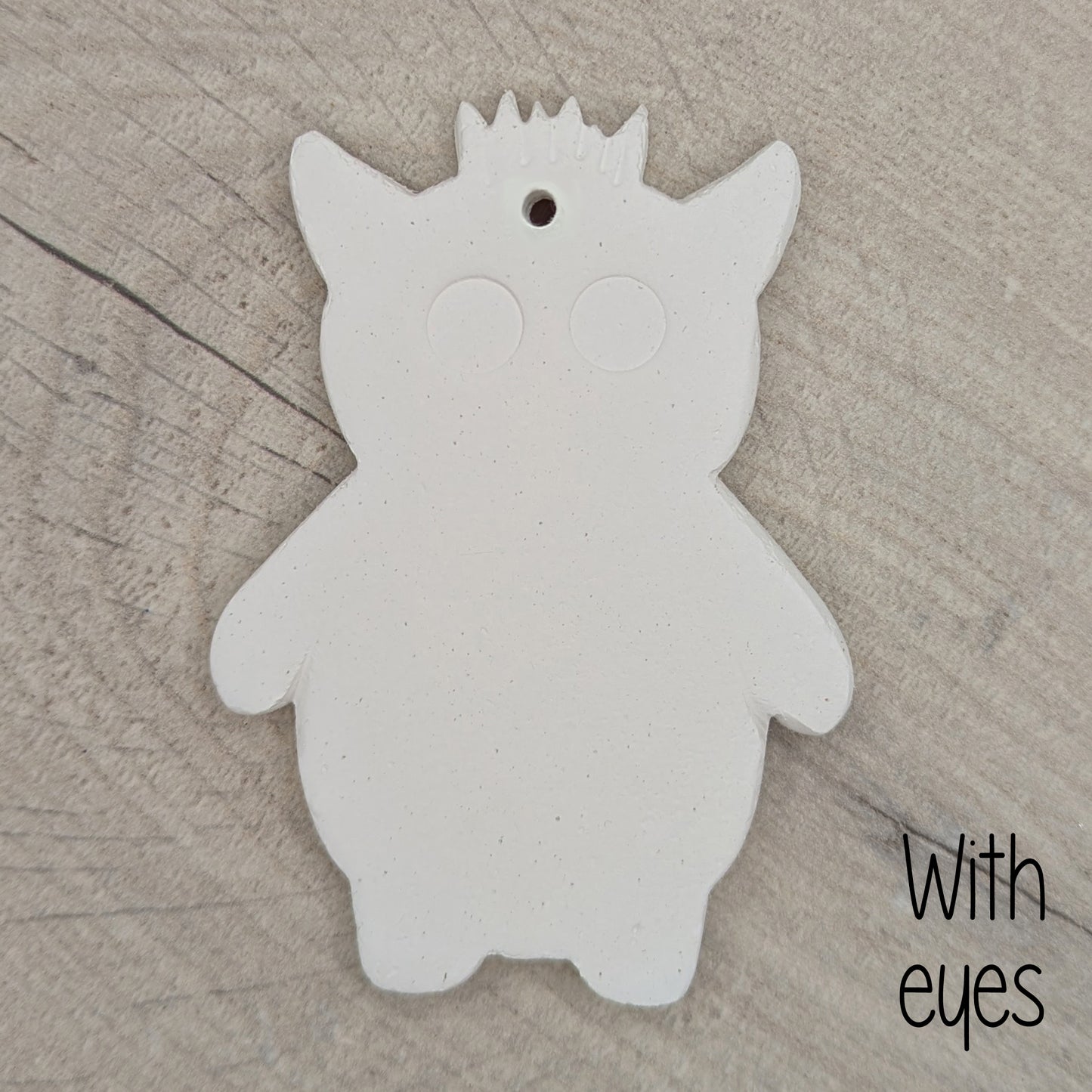 White silhouette of a funky monster with spikey hair, a pointy pair of ears, 2 large round eyes, on a wooden surface