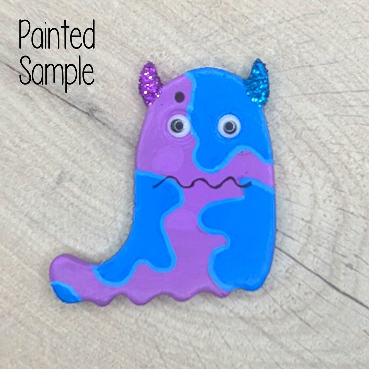 painted sample of ghost monster decoration, painted in blue and lilac with boggle eyes and glitter horns and a squiggly mouth