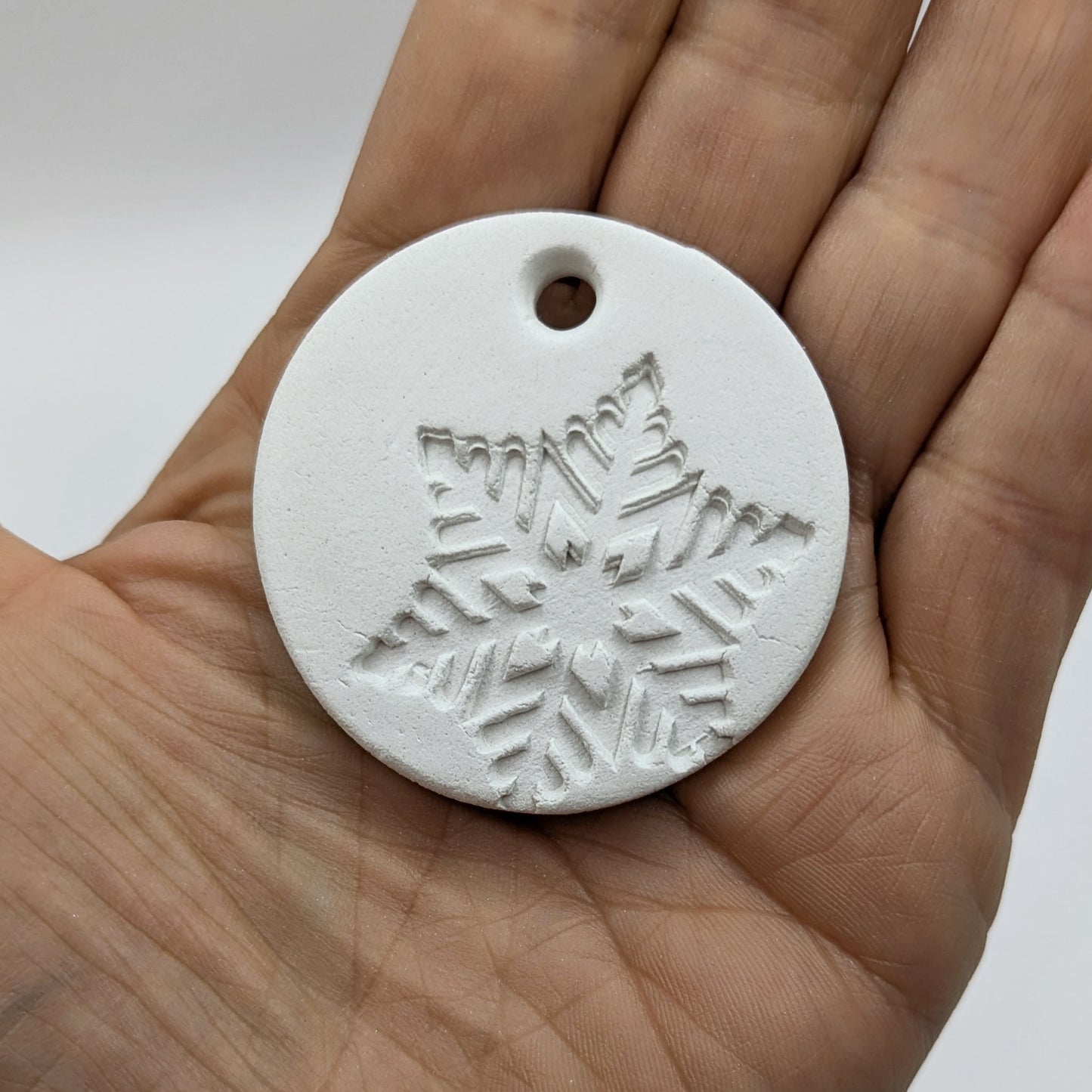 White clay snowflake tag held in a hand