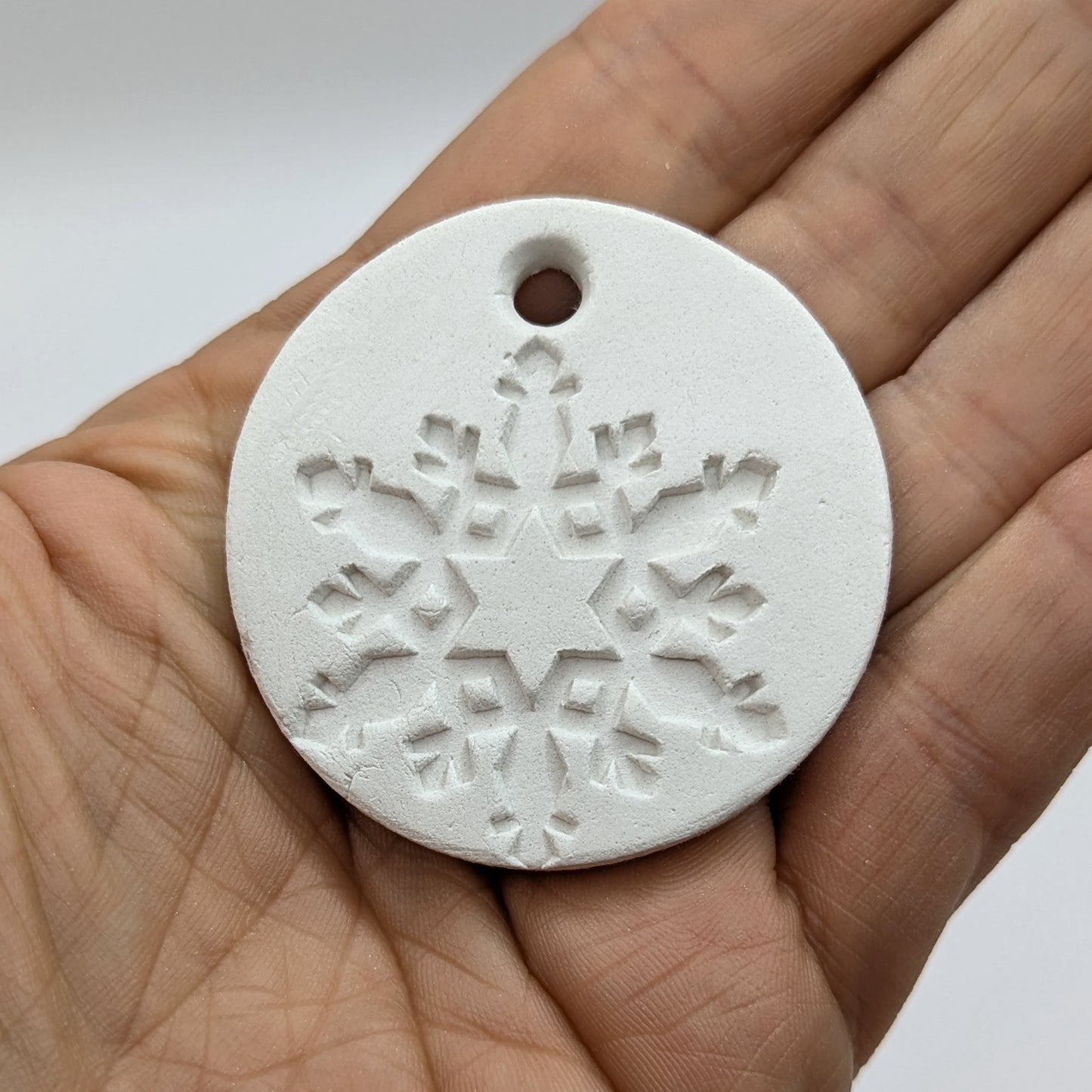 White clay snowflake tag held in a hand