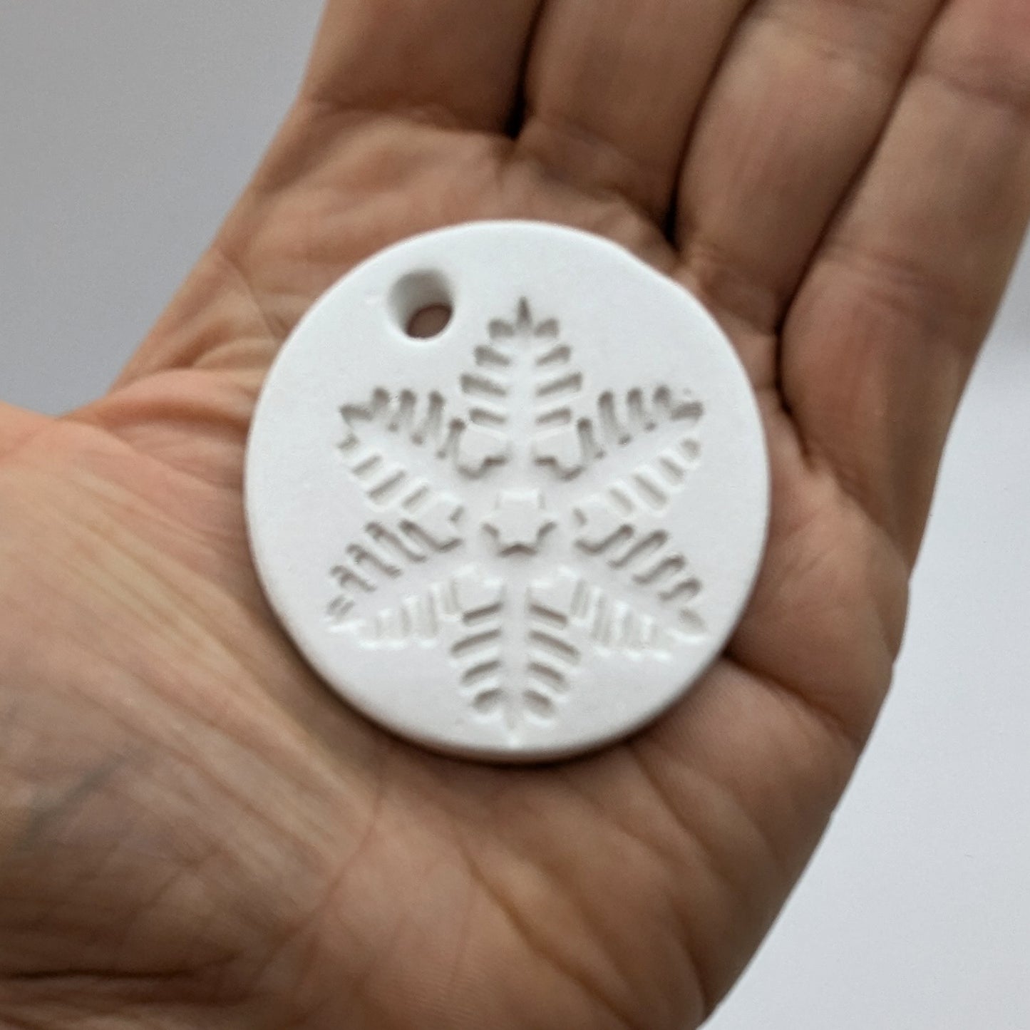 White clay snowflake tag held in a hand