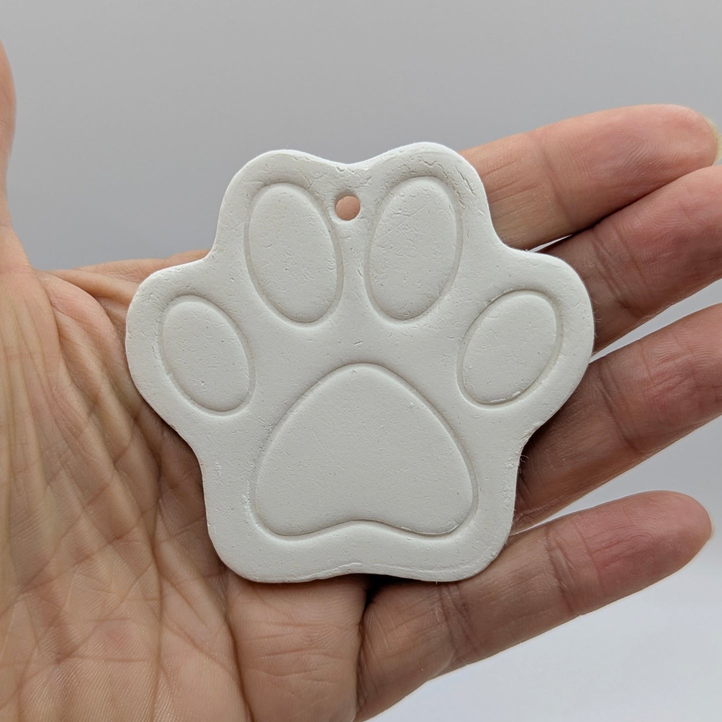 White paw print clay decoration held in a hand against a gray background