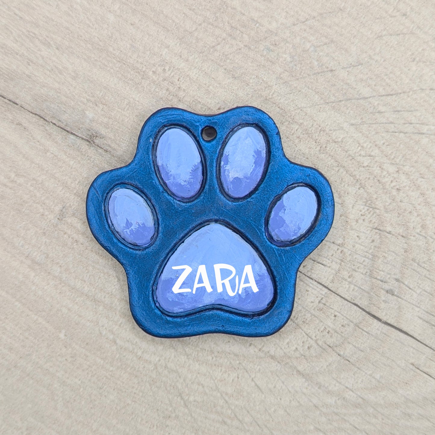 Blue painted paw-shaped clay decoration with 'ZARA' painted onto it