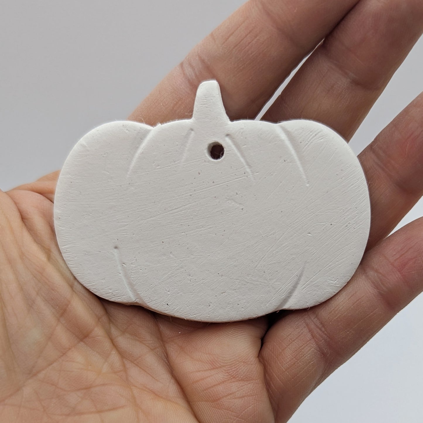 White air dried clay pumpkin ornament held in a hand