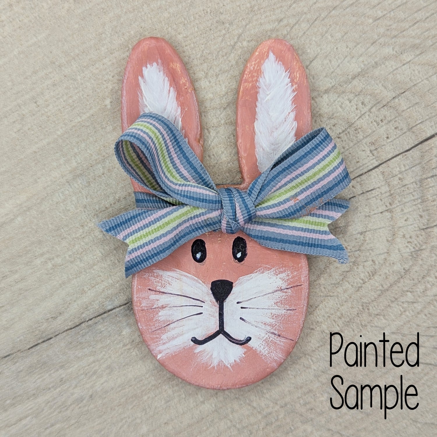 painted rabbit face clay decoration, painted in pastel peach / pink with a blue striped ribbon around the top of the head