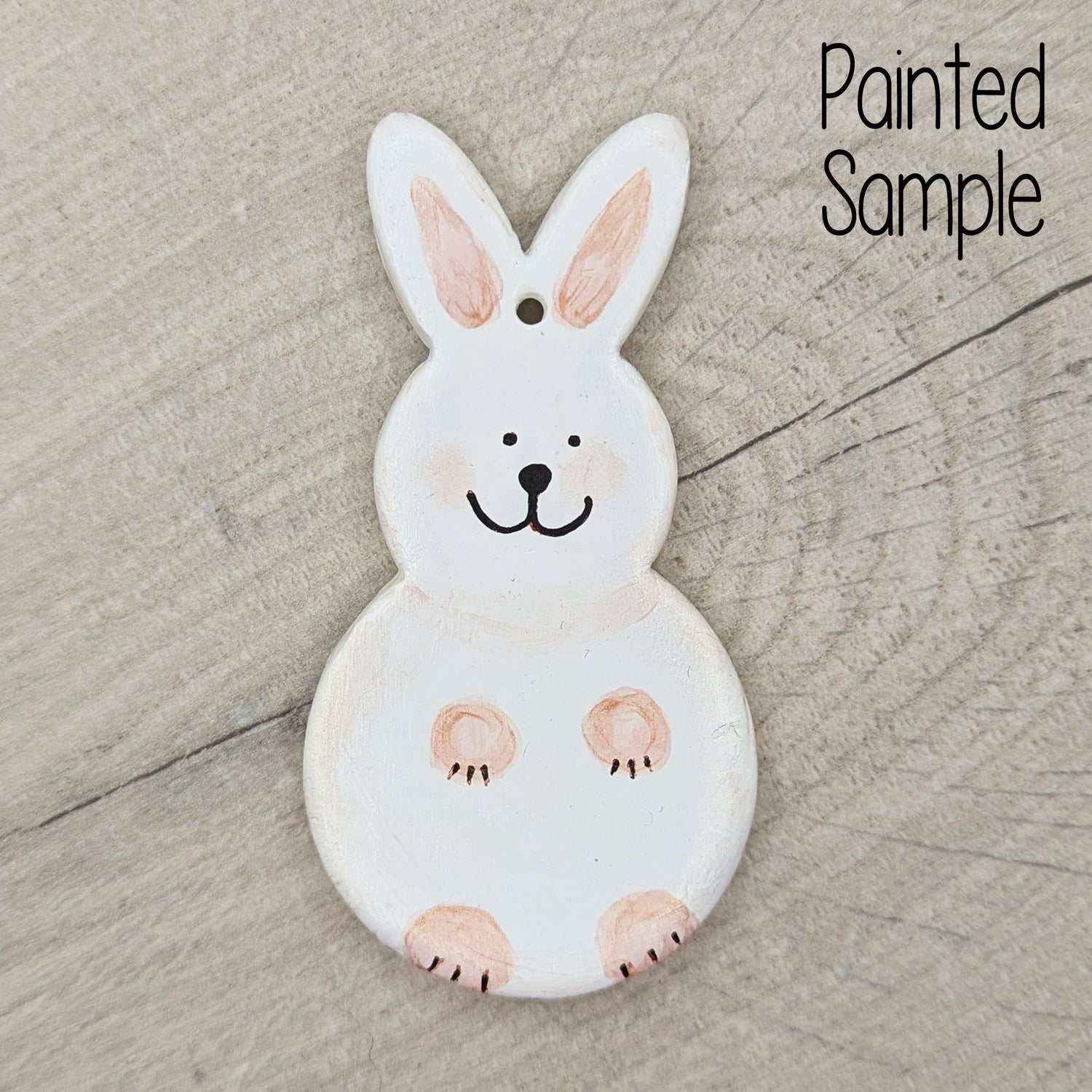 sample of a painted rabbit clay decoration, painted in off white with peach paws and a cute black smiling face