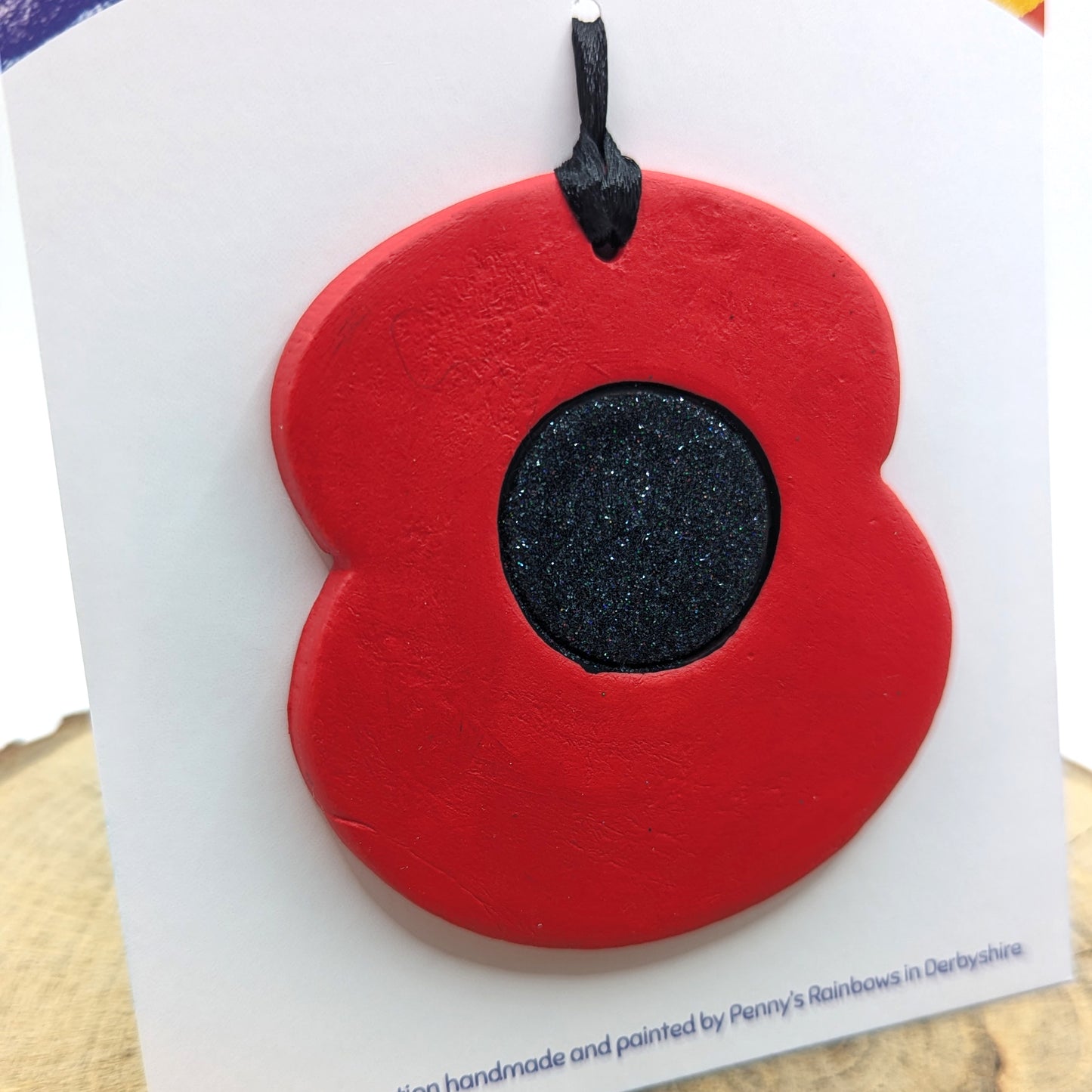 painted poppy clay decoration in red and black displayed on backing card