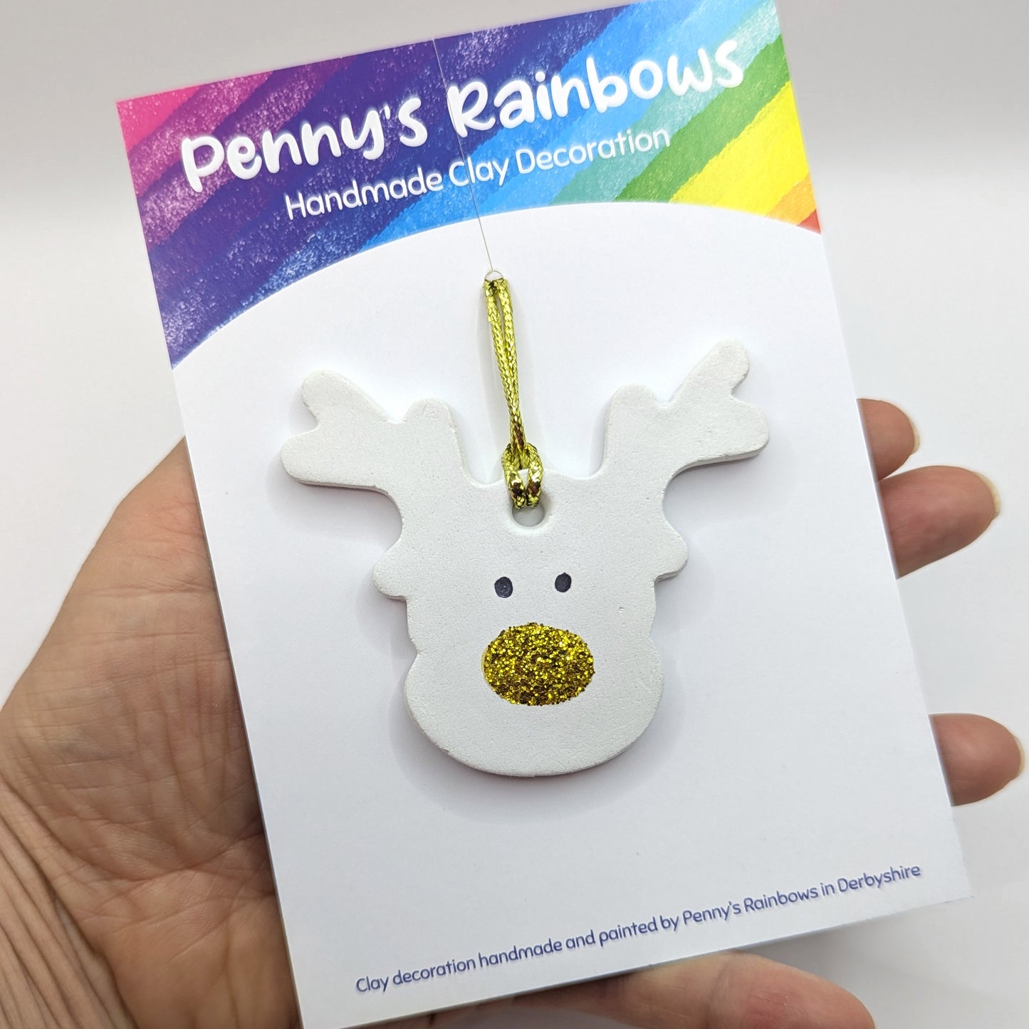 White clay reindeer decoration with gold glitter nose on a card labeled 'Penny's Rainbows'