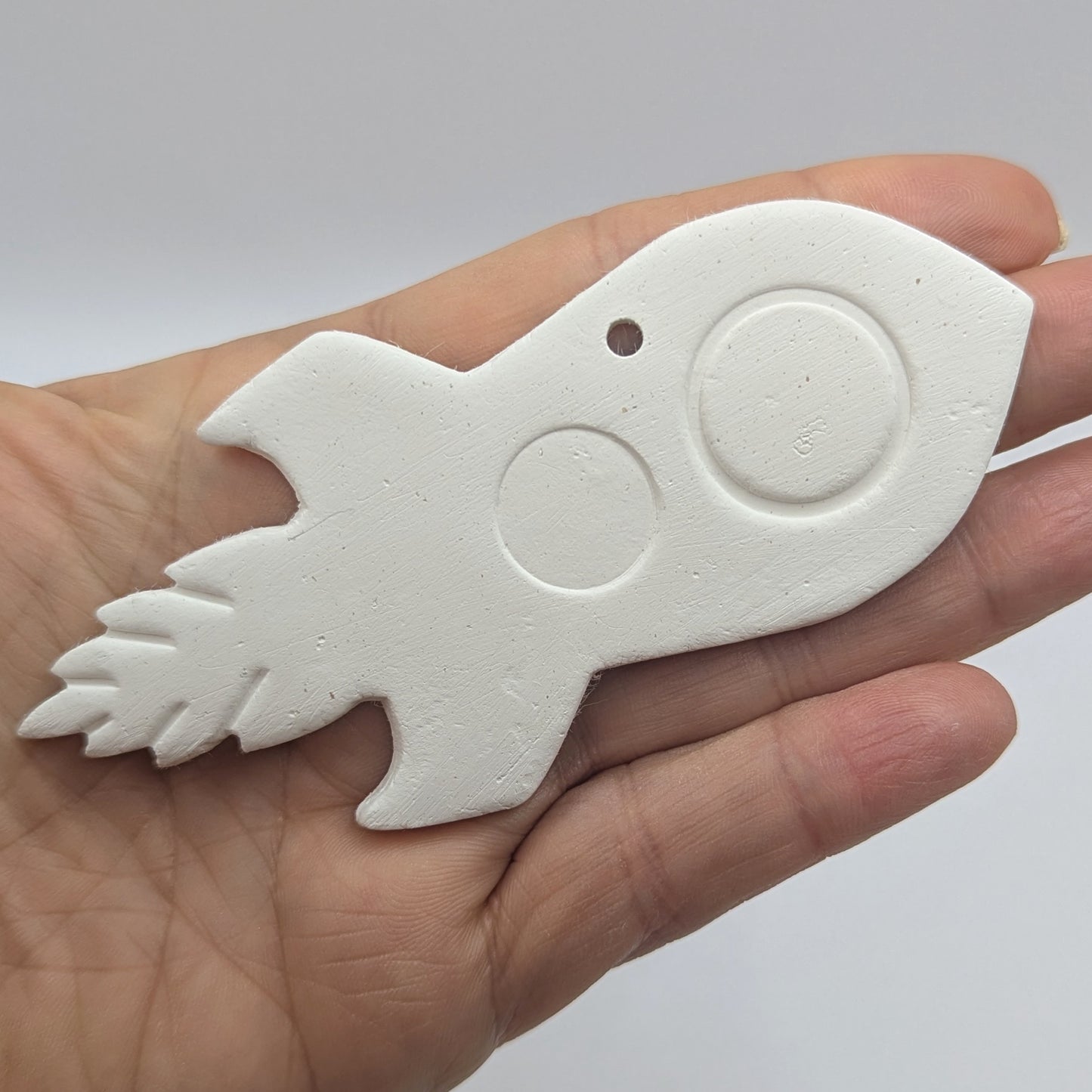 air dried clay decoration in the shape of a rocket, shown in hand for scale