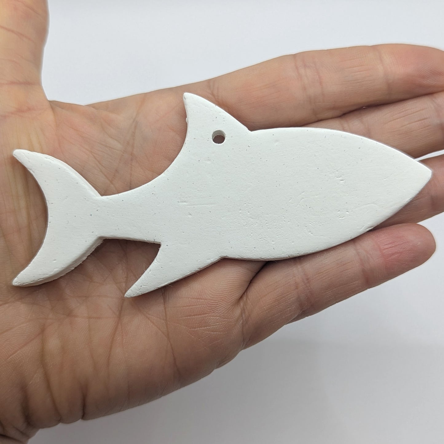 white air dried clayed decoration in the shape of a shark, held in hand to show scale
