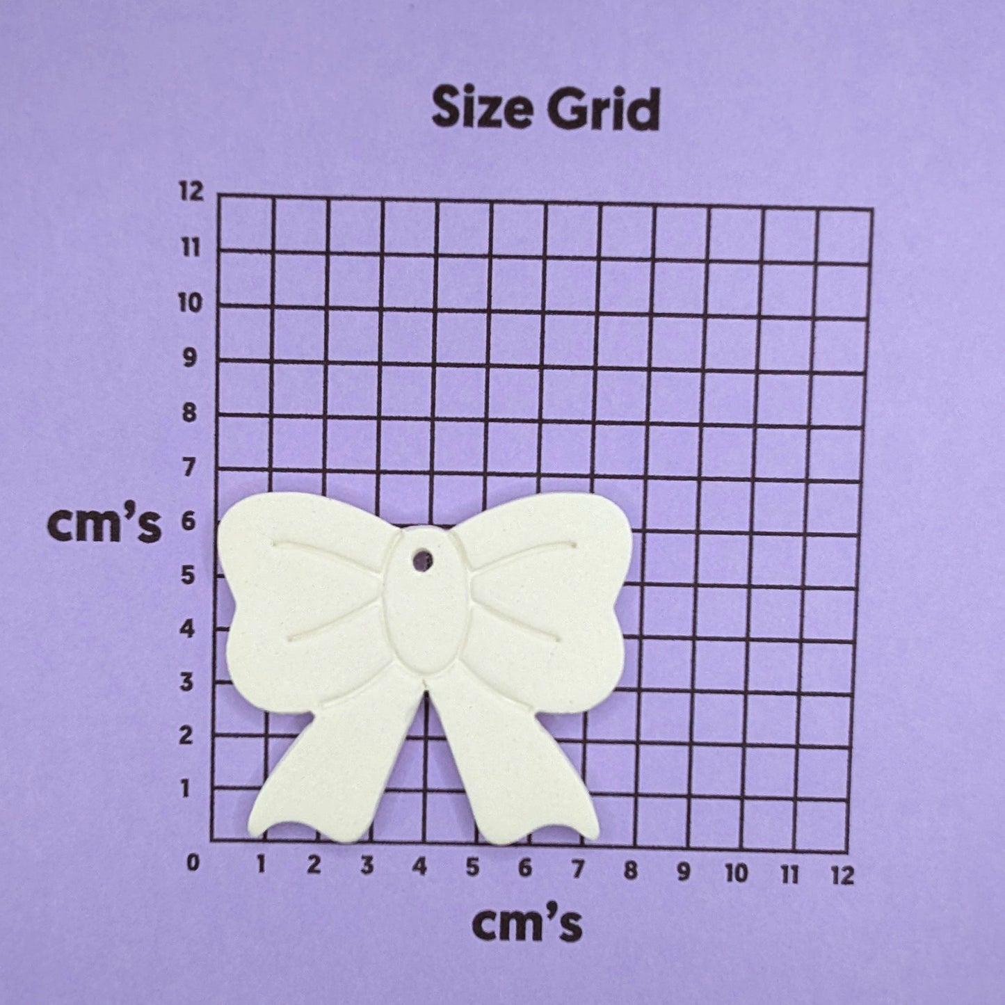 White bow-shaped decoration on a size grid with centimeter markings on a purple background