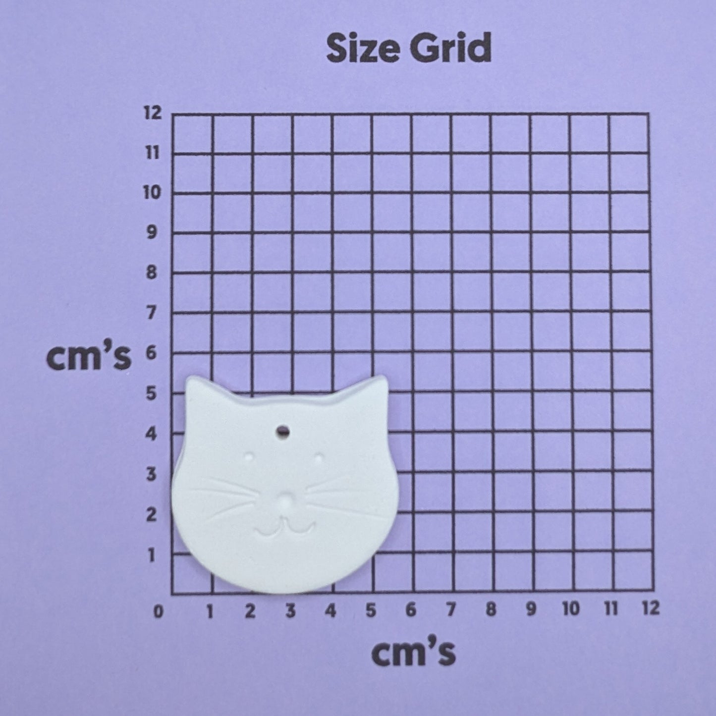 clay small cat face decoration on a size grid with measurements in centimeters