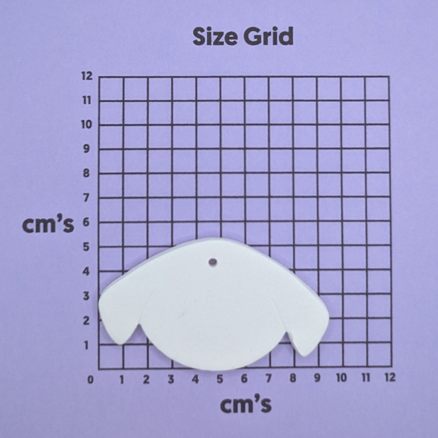 clay dog face decoration on a size grid with measurements in centimeters