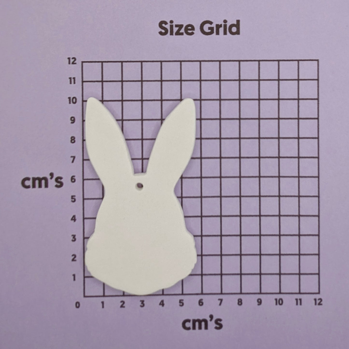 White bunny-shaped decoration on a size grid with centimeter markings on a purple background