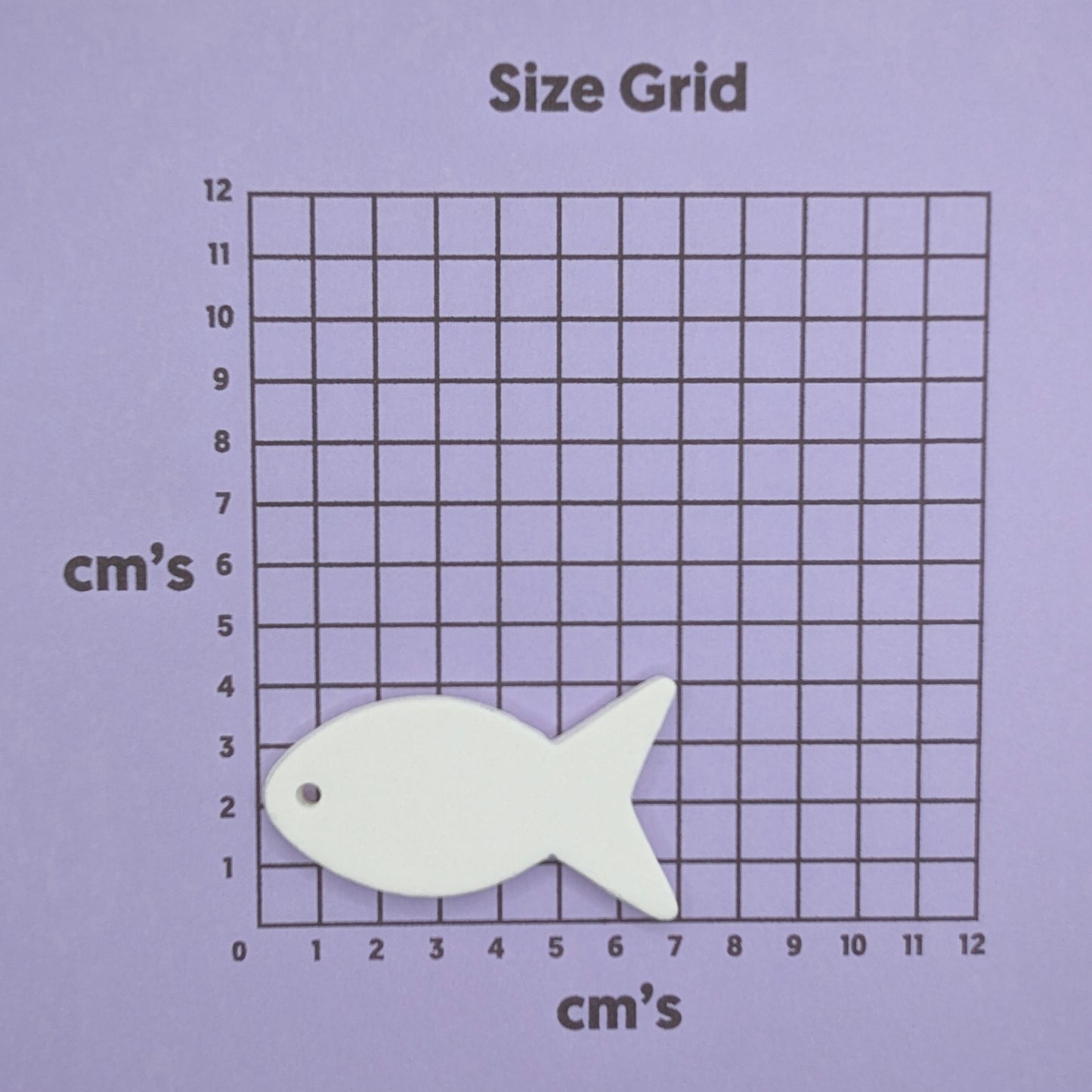 White fish-shaped clay decoration on a size grid with centimeter markings on a purple background