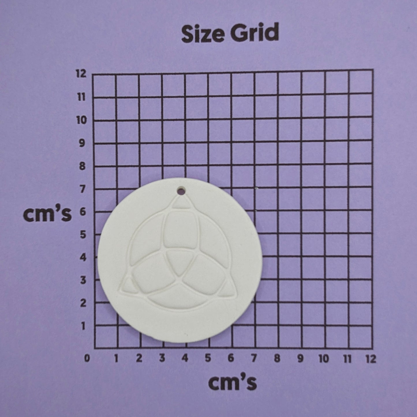 white air dried clay decoration with the triquetra symbol stamped into it shown on a size grid to show size