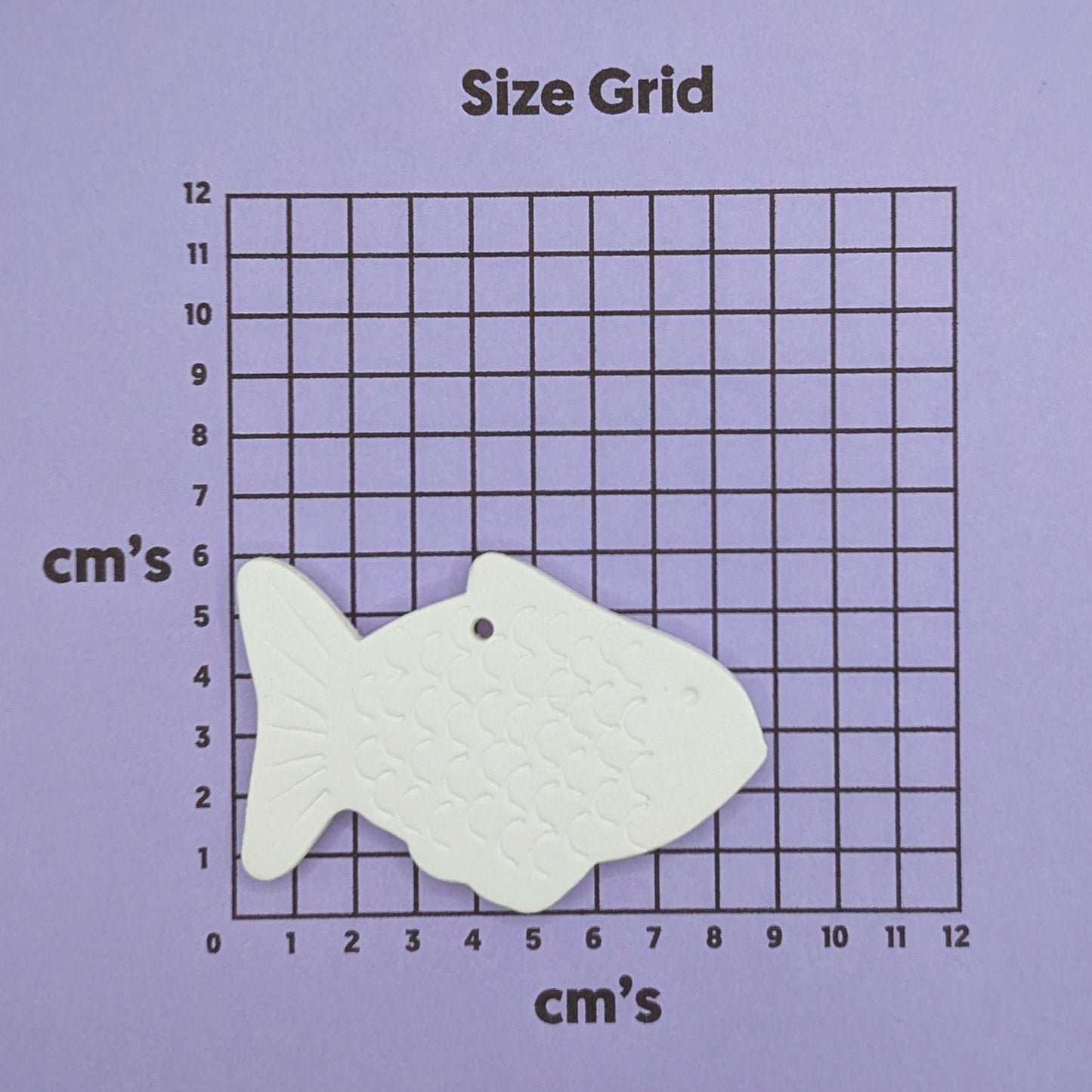 White gold fish-shaped clay decoration on a purple size grid with 'cm's' labels