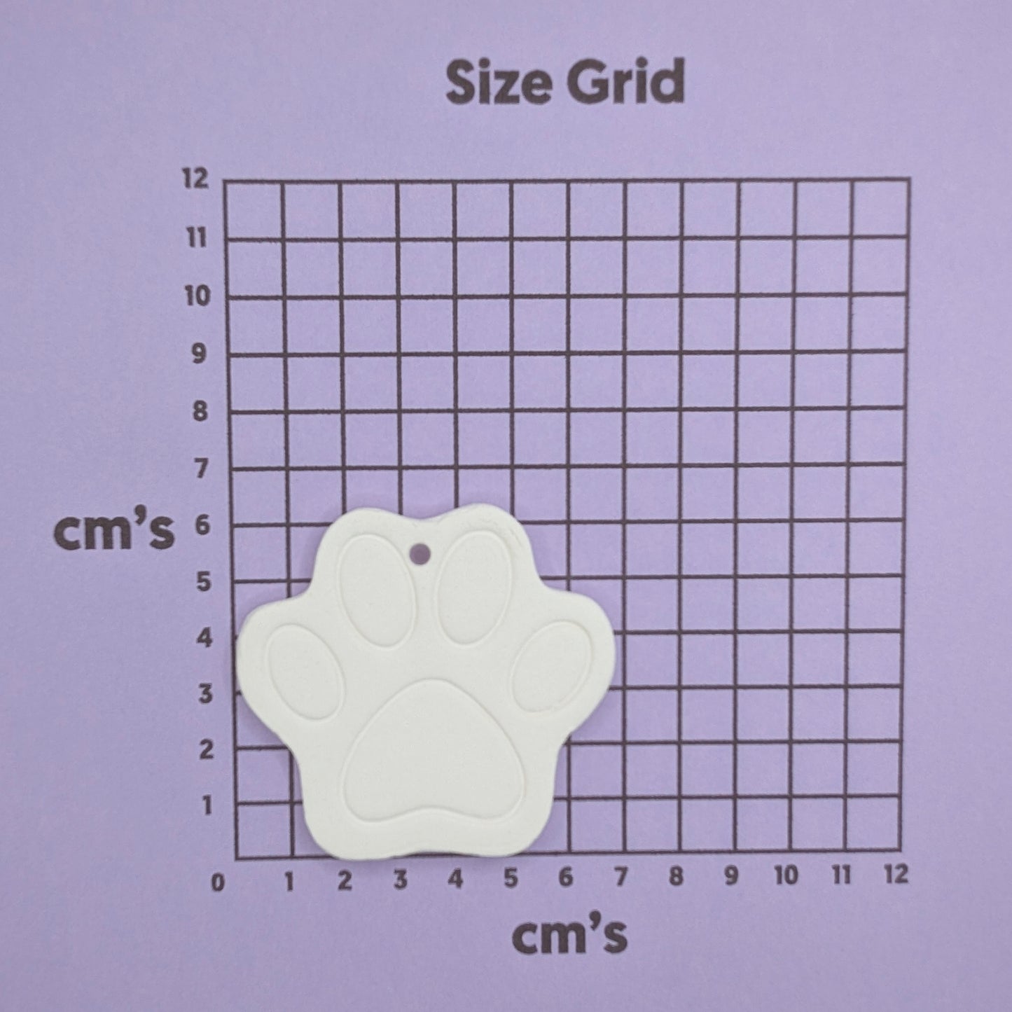 White paw-shaped clay decoration on a size grid with centimeter measurements on a purple background