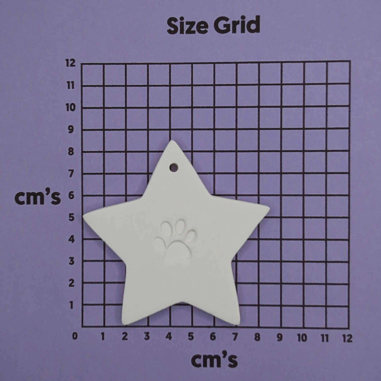 Star shaped clay decoration with a paw print design in the centre shown on a purple size grid to show size