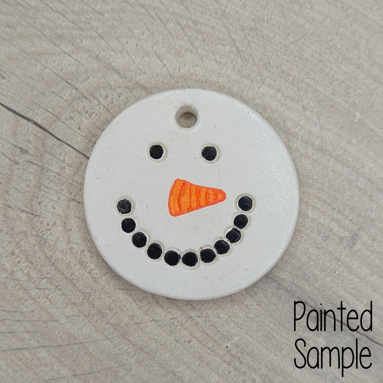painted snowman face on clay decoration, black for coal mouth and eyes and orange triangle for carrot nose