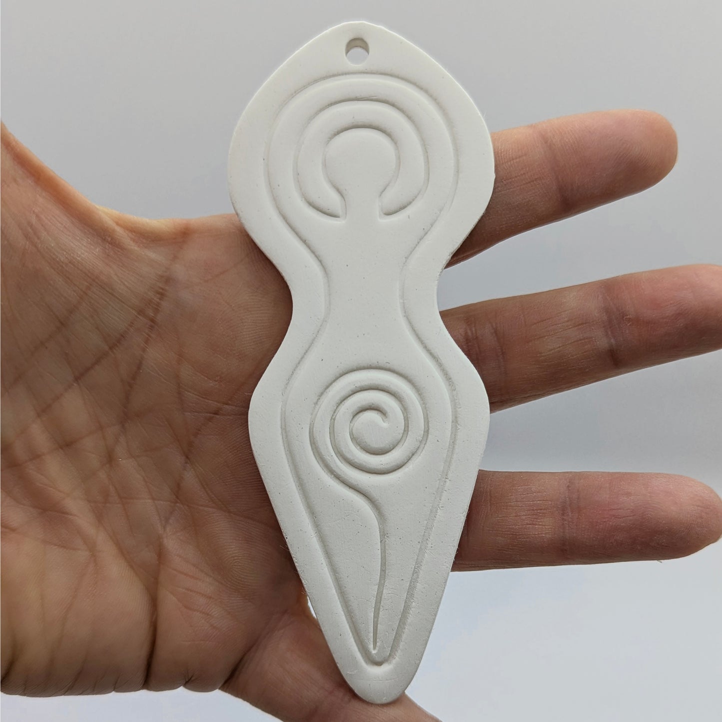 Spiral goddess shaped clay decoration shown on in some ones hand for scale