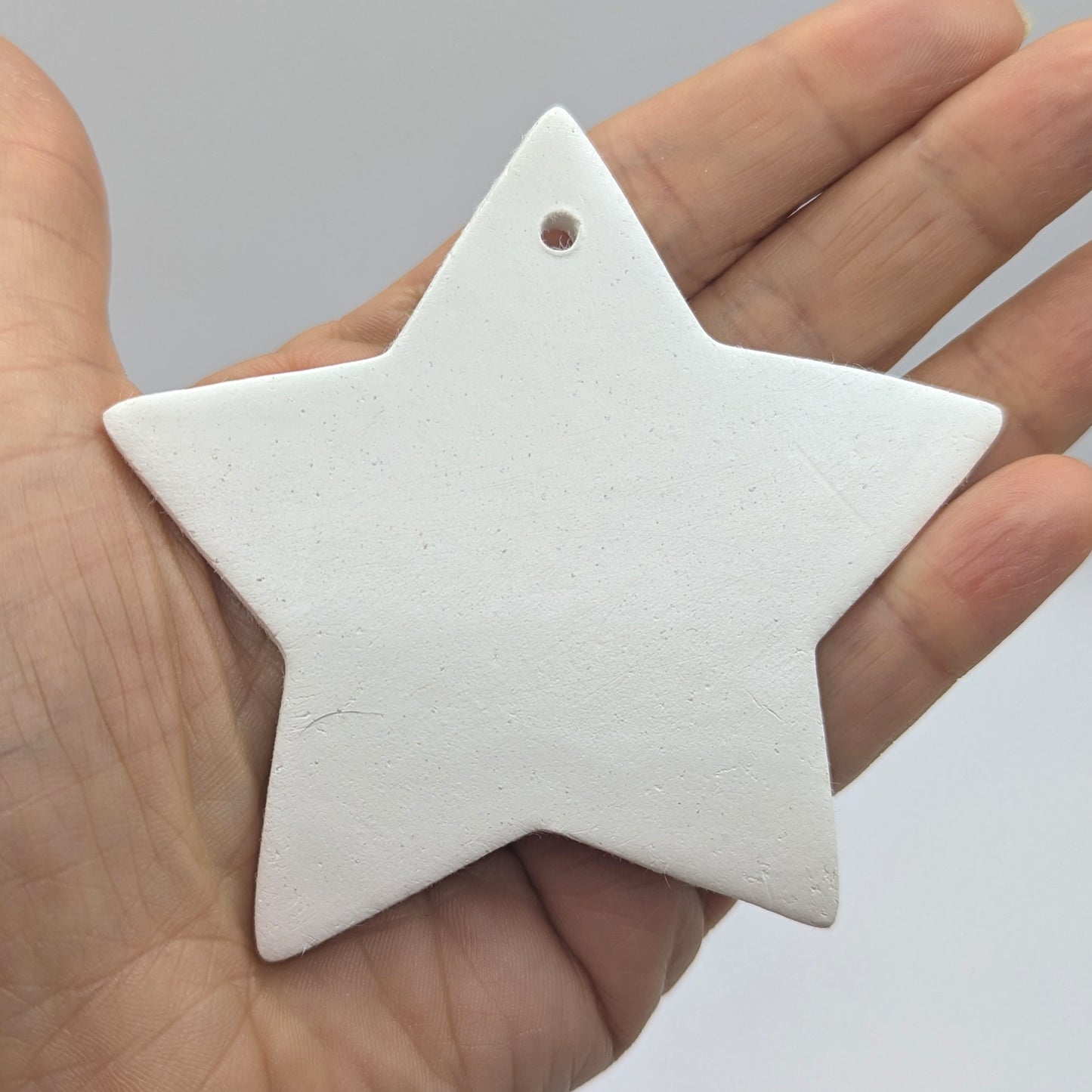 White 5 pointed star shaped clay decoration / ornament/ tag, held in a hand against a gray background