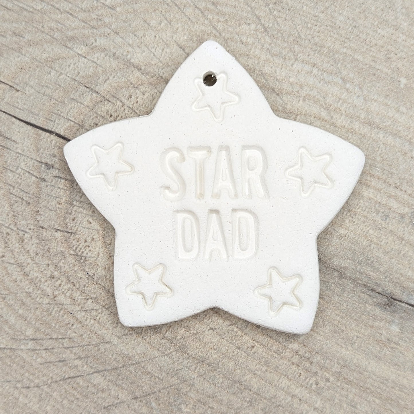 Star shaped white clay decoration / ornament with 'STAR DAD' text on a wooden surface