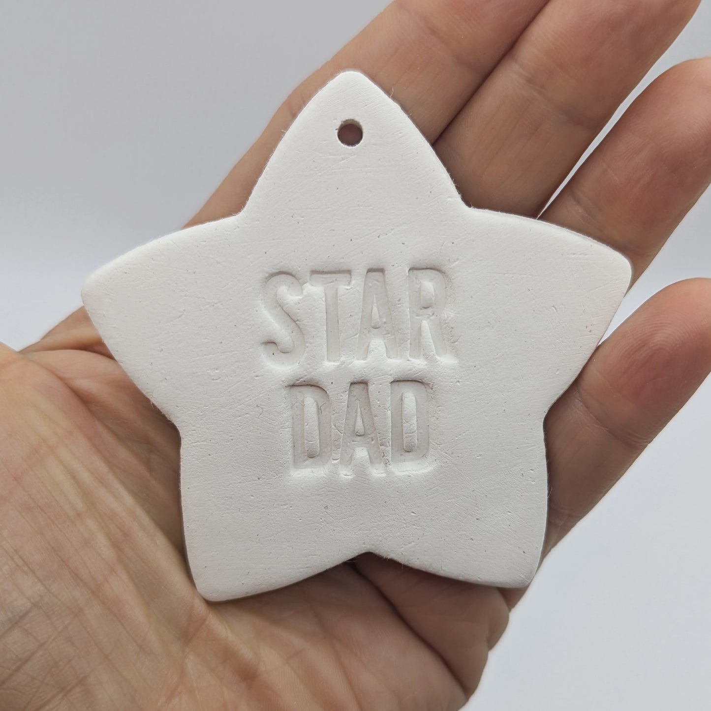 White clay 5 pointed star ornament / decoration with 'Star Dad' stamped into the clay, held in a hand to show scale
