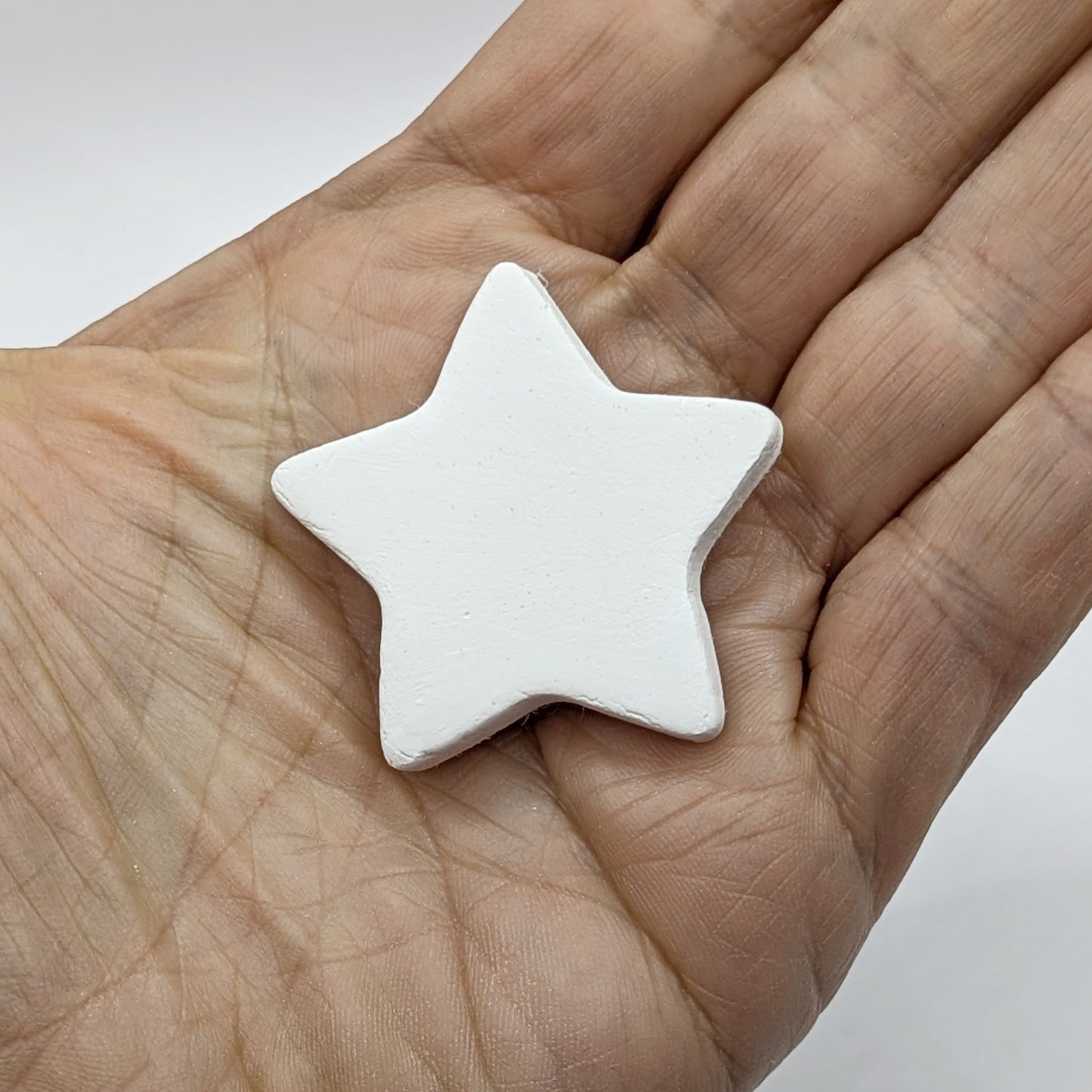 white air dried clay mini star decoration shown in palm of hand