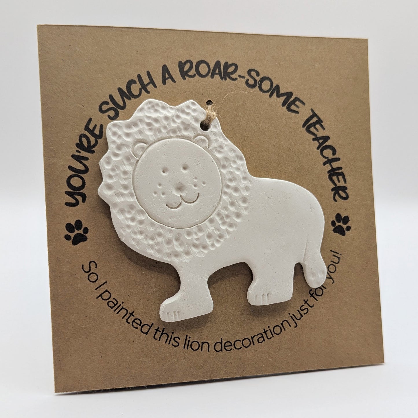 'You're such a roar-some teacher' text on a brown kraft card with a clay lion decoration attached for you to paint and decorate