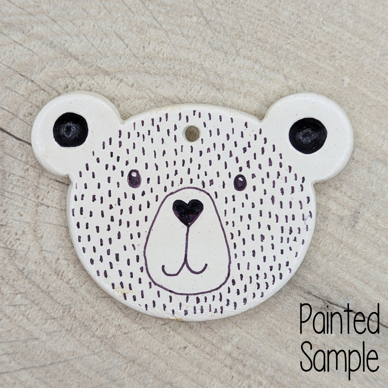 teddy bear face clay decoration, decorated in just black sharpie pen with a heart shaped nose and smiley mouth