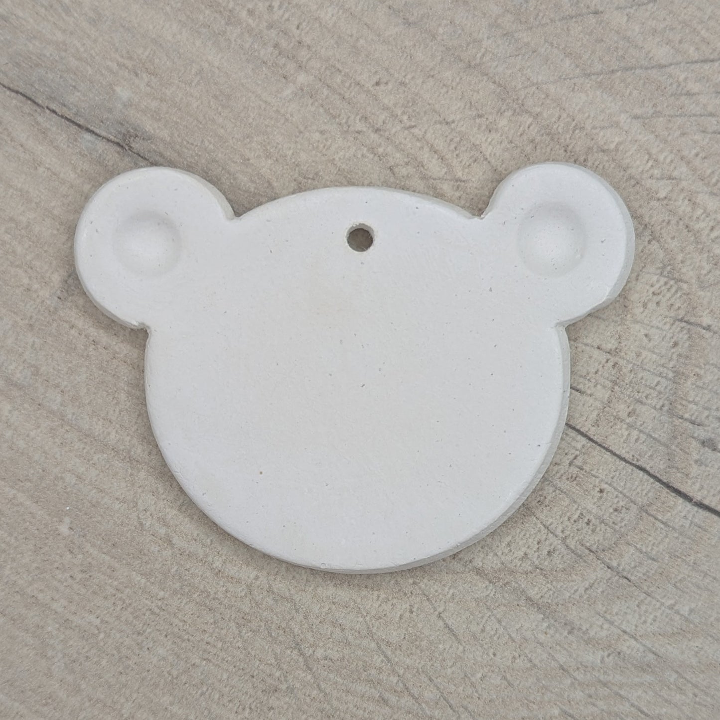 White clay decoration in the shape of a teddy bear head with ears stamped in on a wooden surface