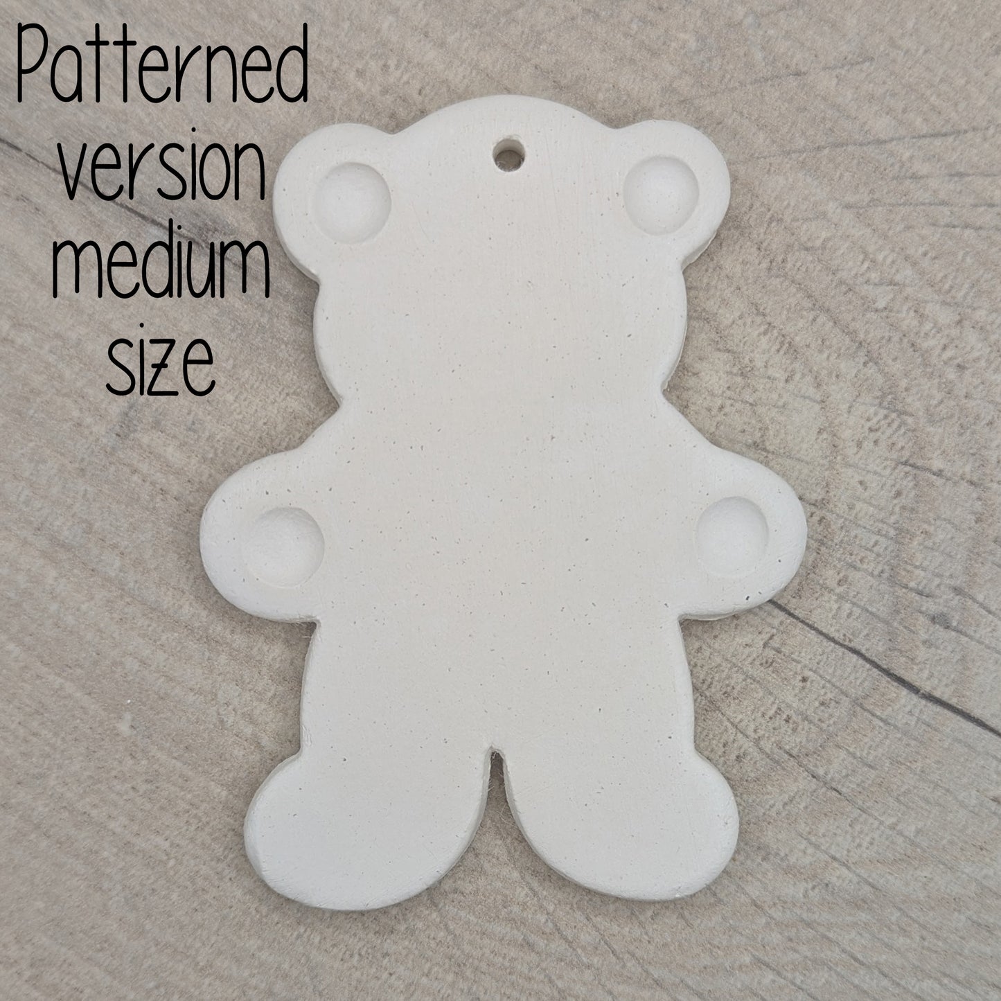 White clay decoration in the shape of a teddy bear with ears and paws stamped on, on wooden background
