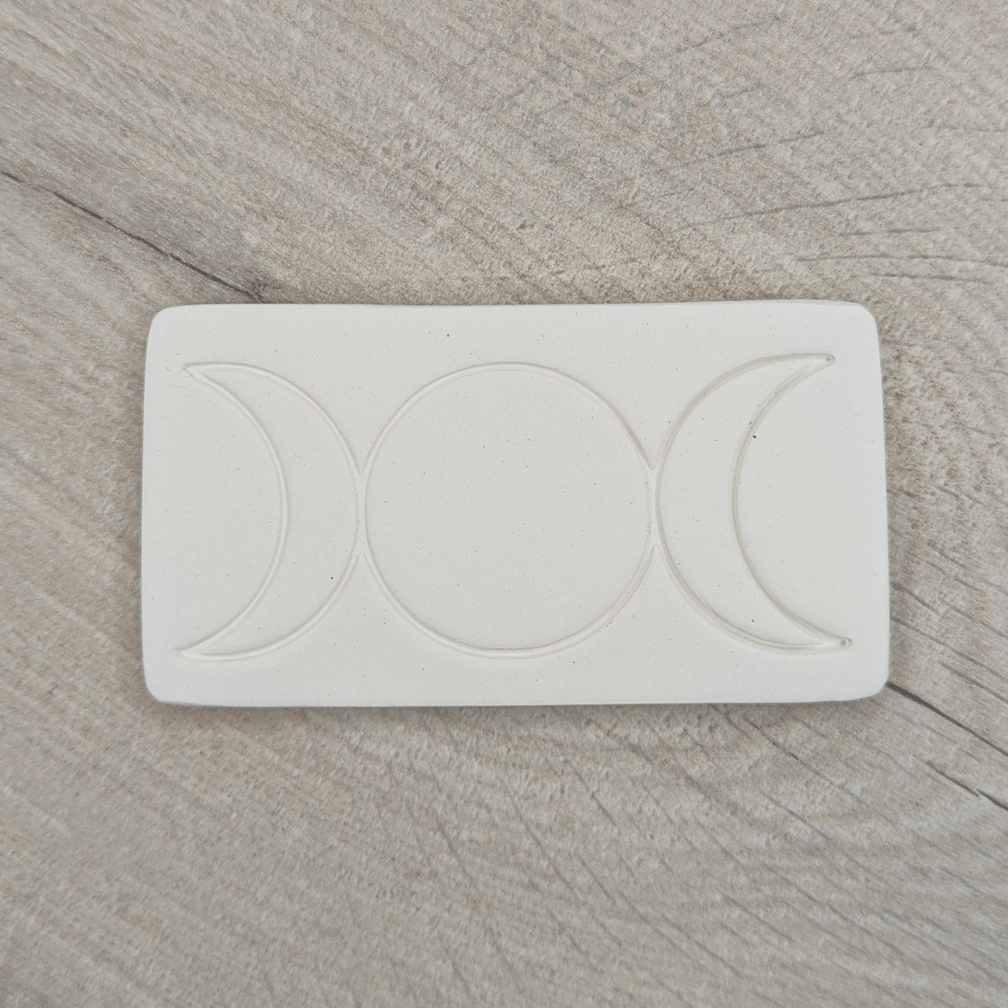rectangular shaped air dried clay decoration with the triple moon symbol stamped into it on a wooden background