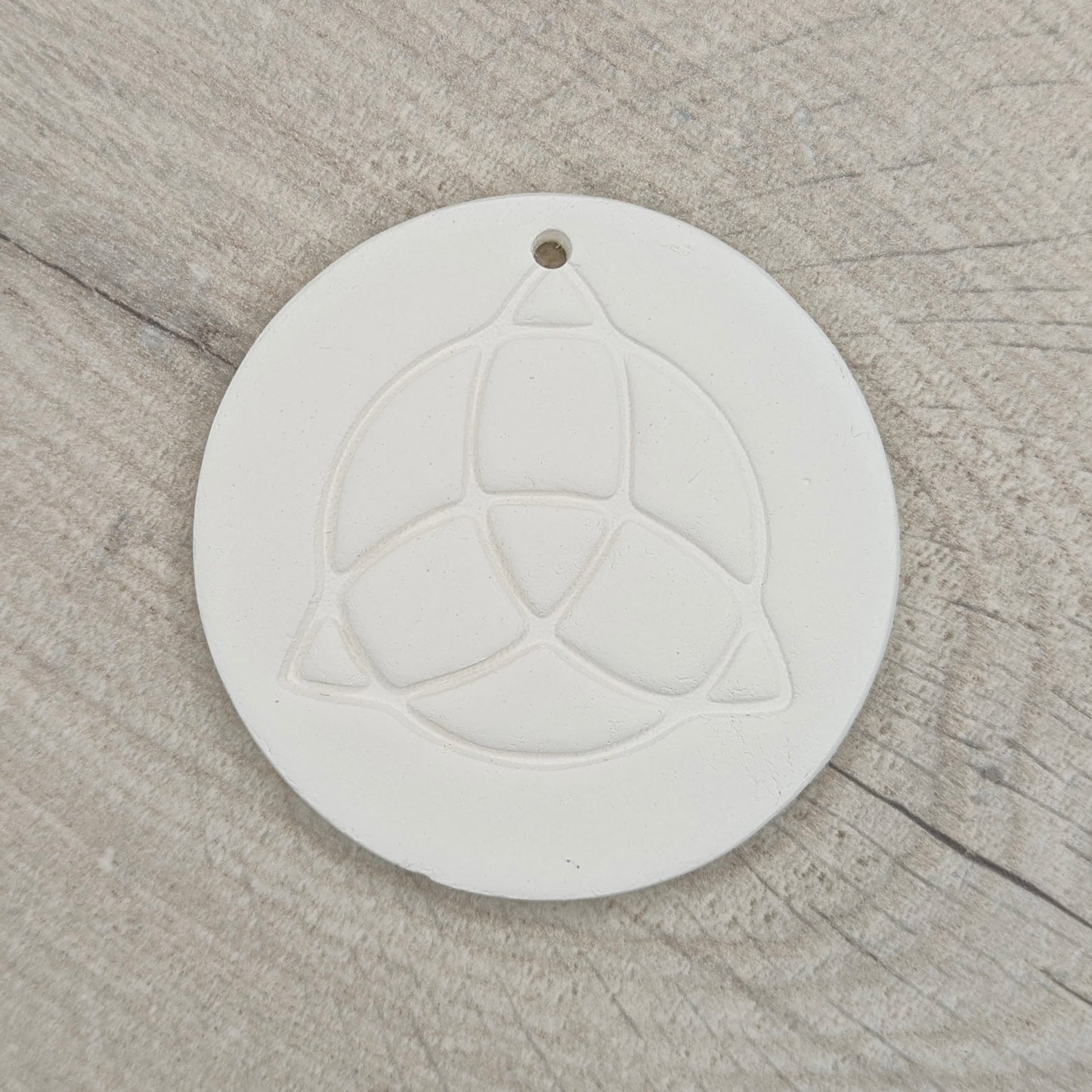 white air dried clay decoration with the triquetra symbol stamped into it on a wooden background