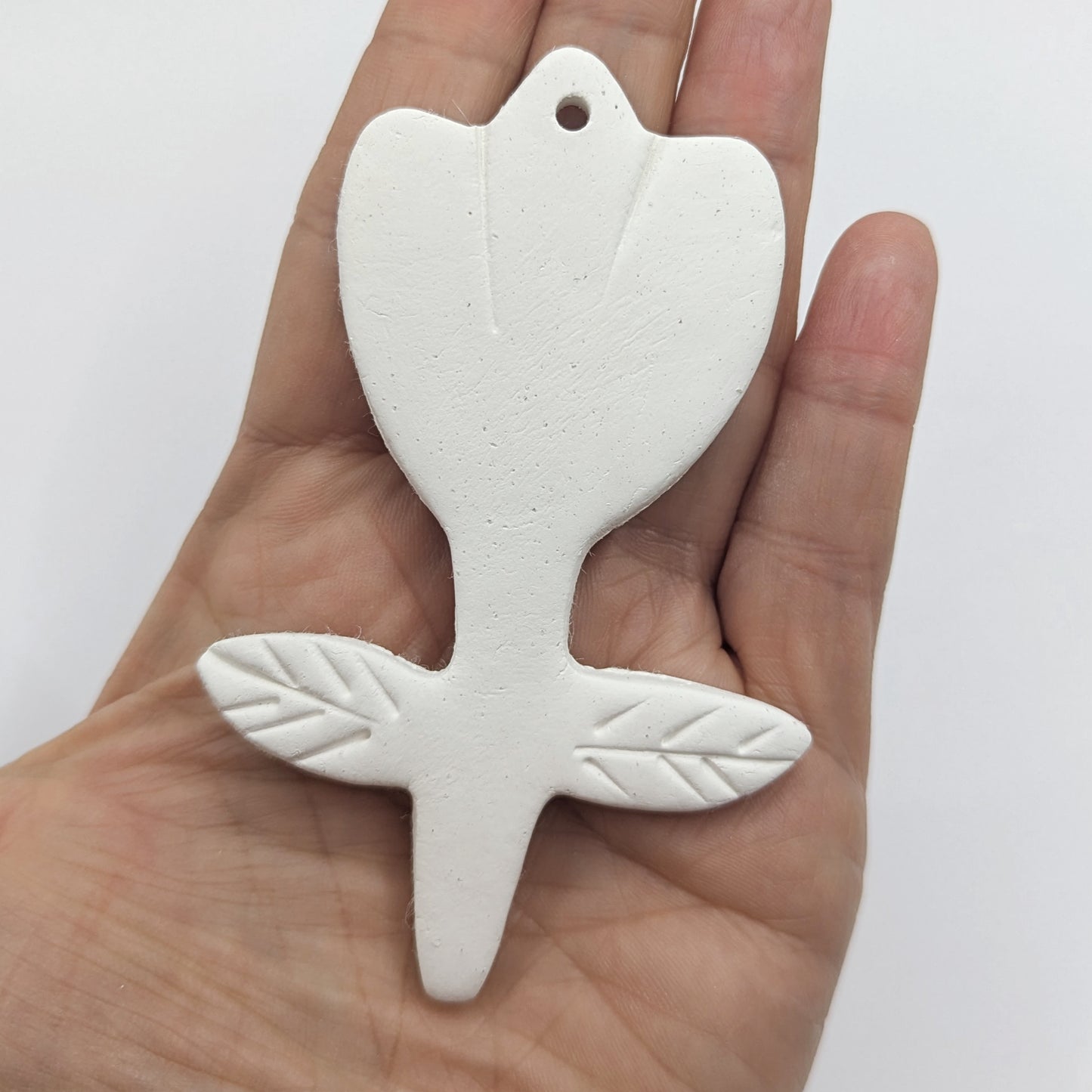 White clay decoration in the shape of a tulip with leaf pattern stamped on, held in hand for scale