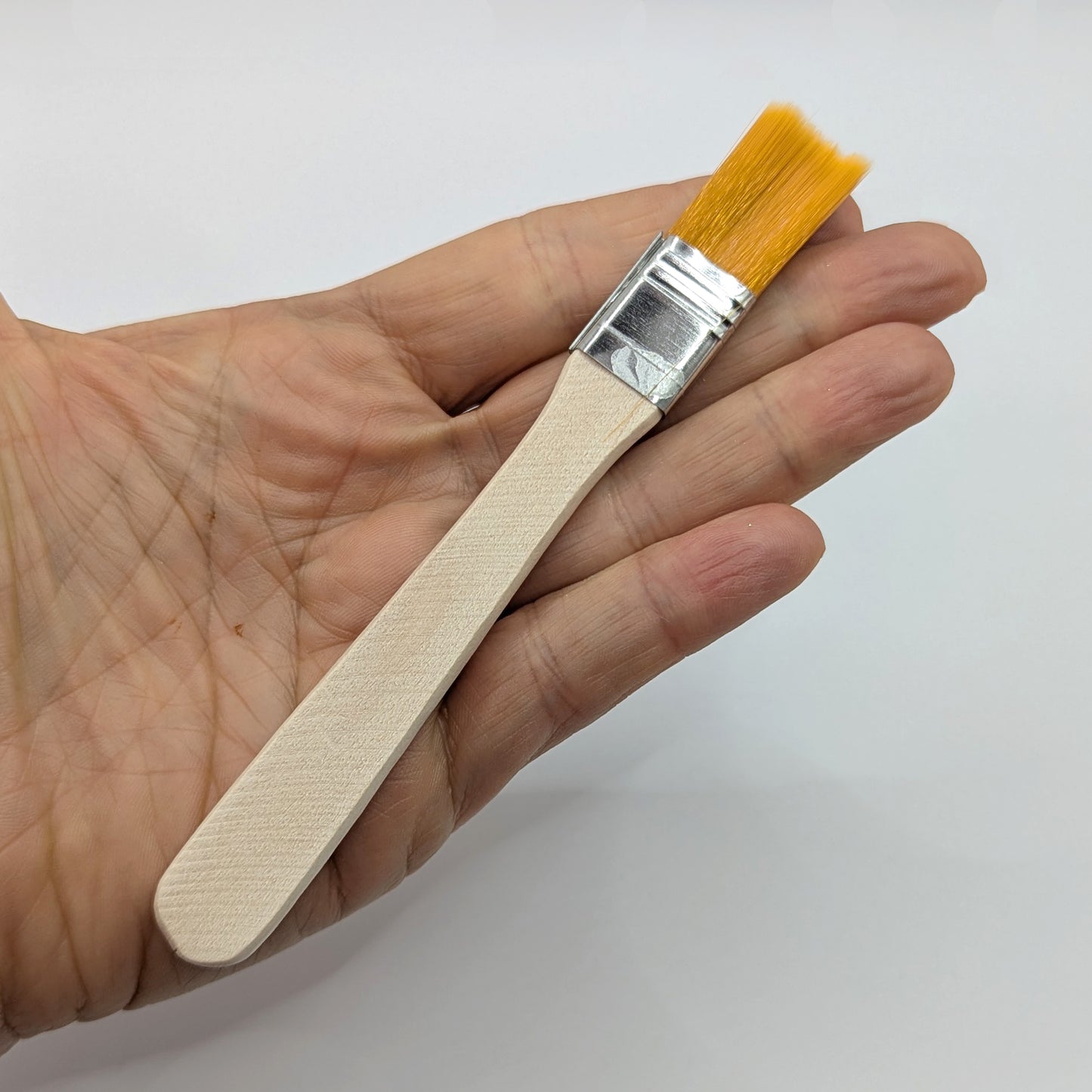 Hand holding a small paintbrush with a wooden handle and yellow bristles